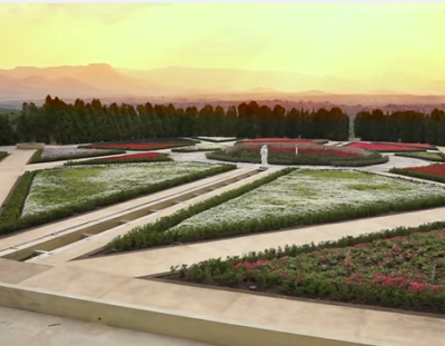 fotografía del jardín estilo italiano al atardecer. Se distinguen un par de estatuas de mármol al fondo, las flores son, en su mayoría, rojas